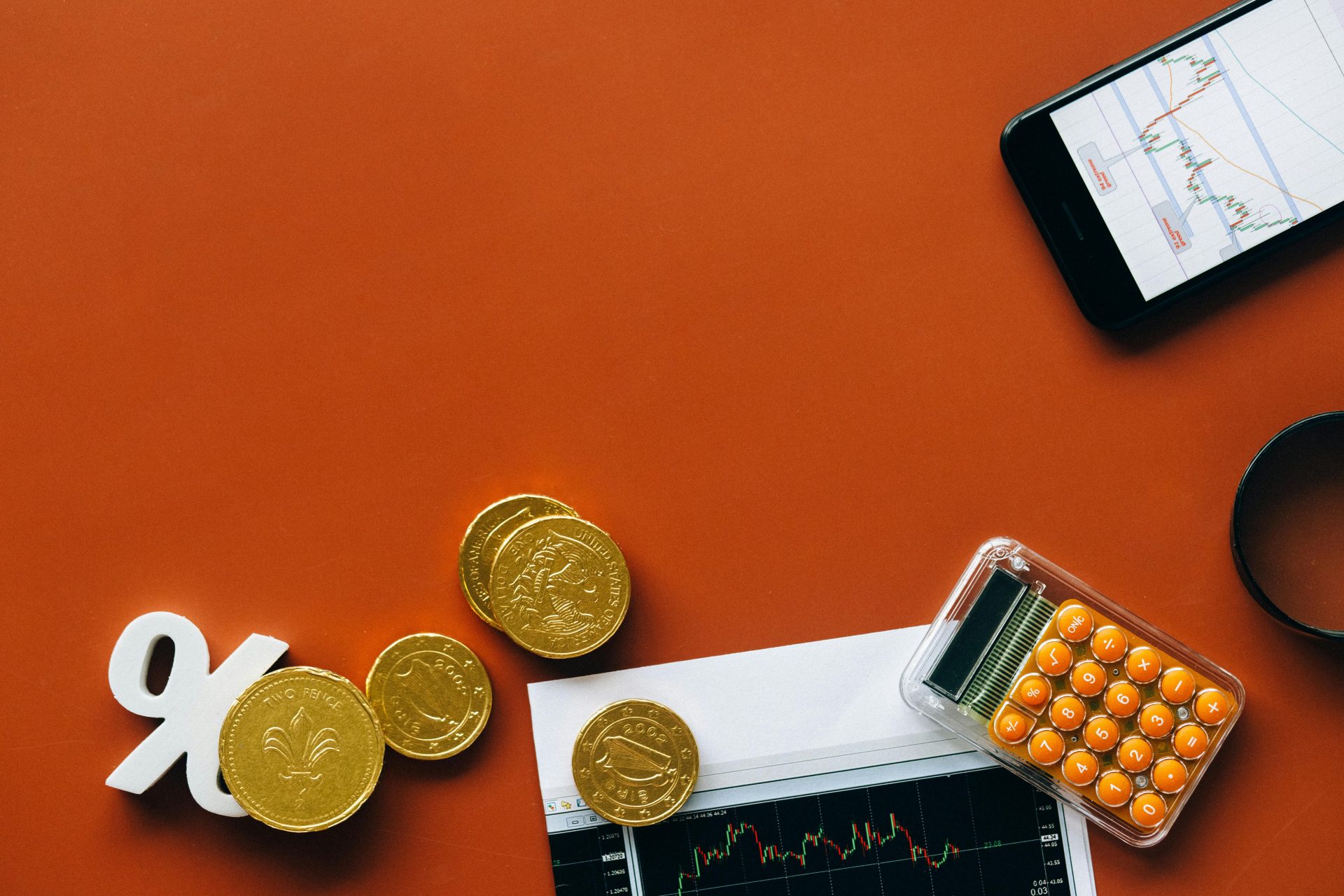 Vue à plat montrant des pièces de monnaie, une calculatrice et des graphiques sur fond rouge pour l'analyse financière et les concepts commerciaux.